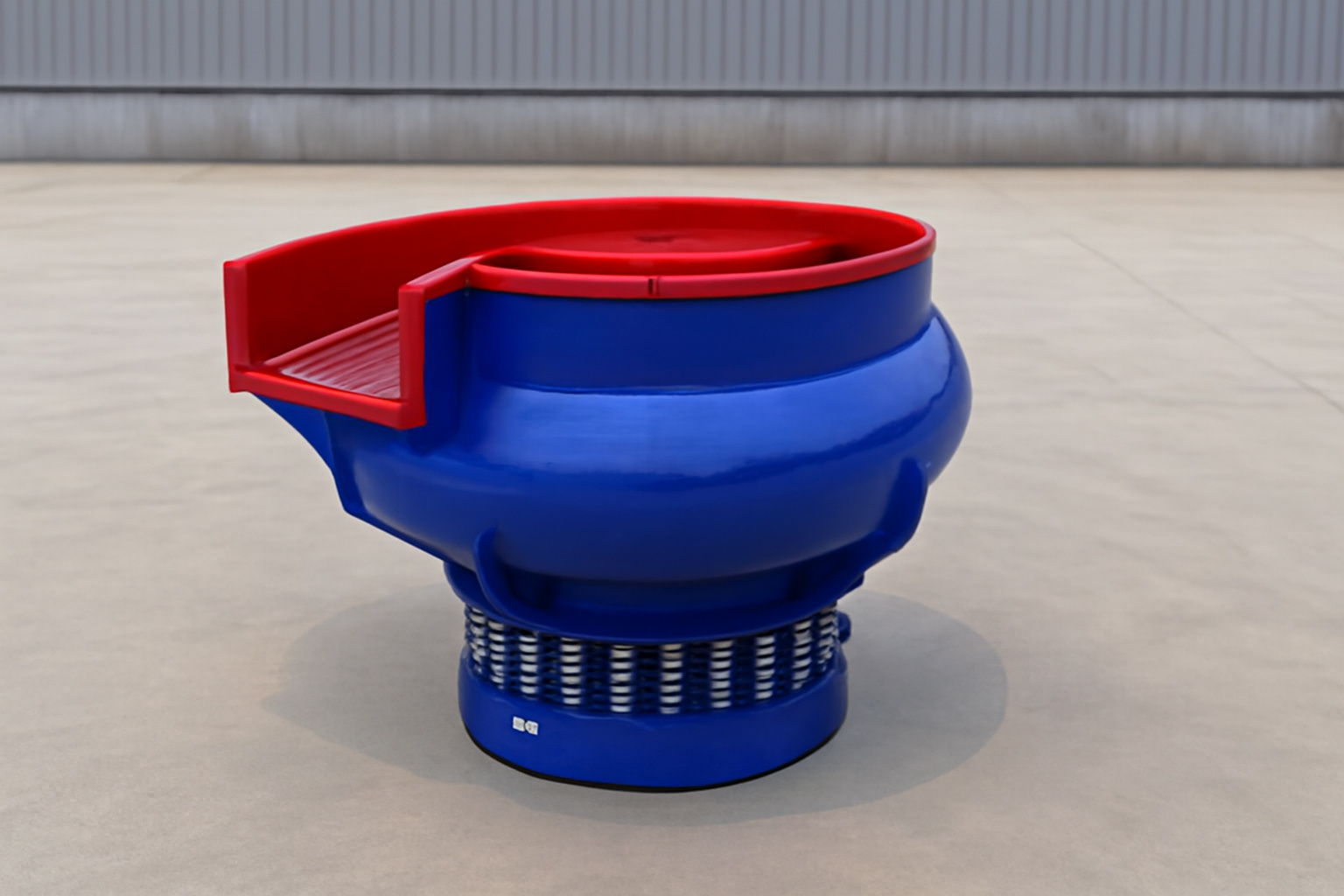 A vibratory bowl finishing machine with a red lip, designed for industrial use, featuring a spring-loaded base and smooth operation on a concrete surface in a factory setting.